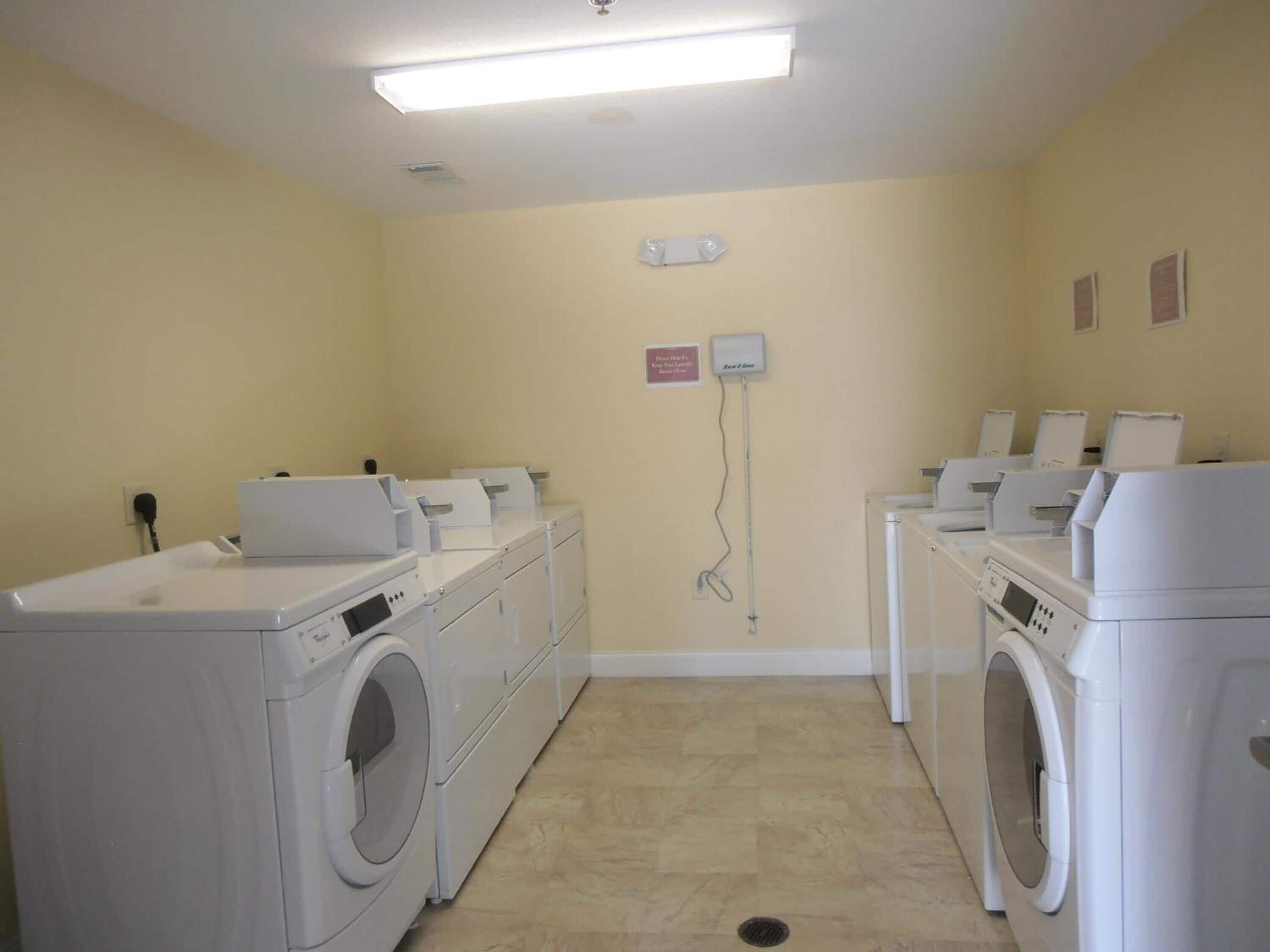 A laundry room with multiple washing machines and dryers, a wall-mounted electrical outlet, and a sign indicating the room's purpose.