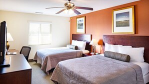 A hotel room with two beds, a desk with a computer, a ceiling fan, and framed pictures on the wall. - Affordable Suites Augusta (Augusta)