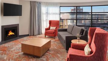 A modern living room with a fireplace, a large flat-screen TV, and a view of a building across the window.