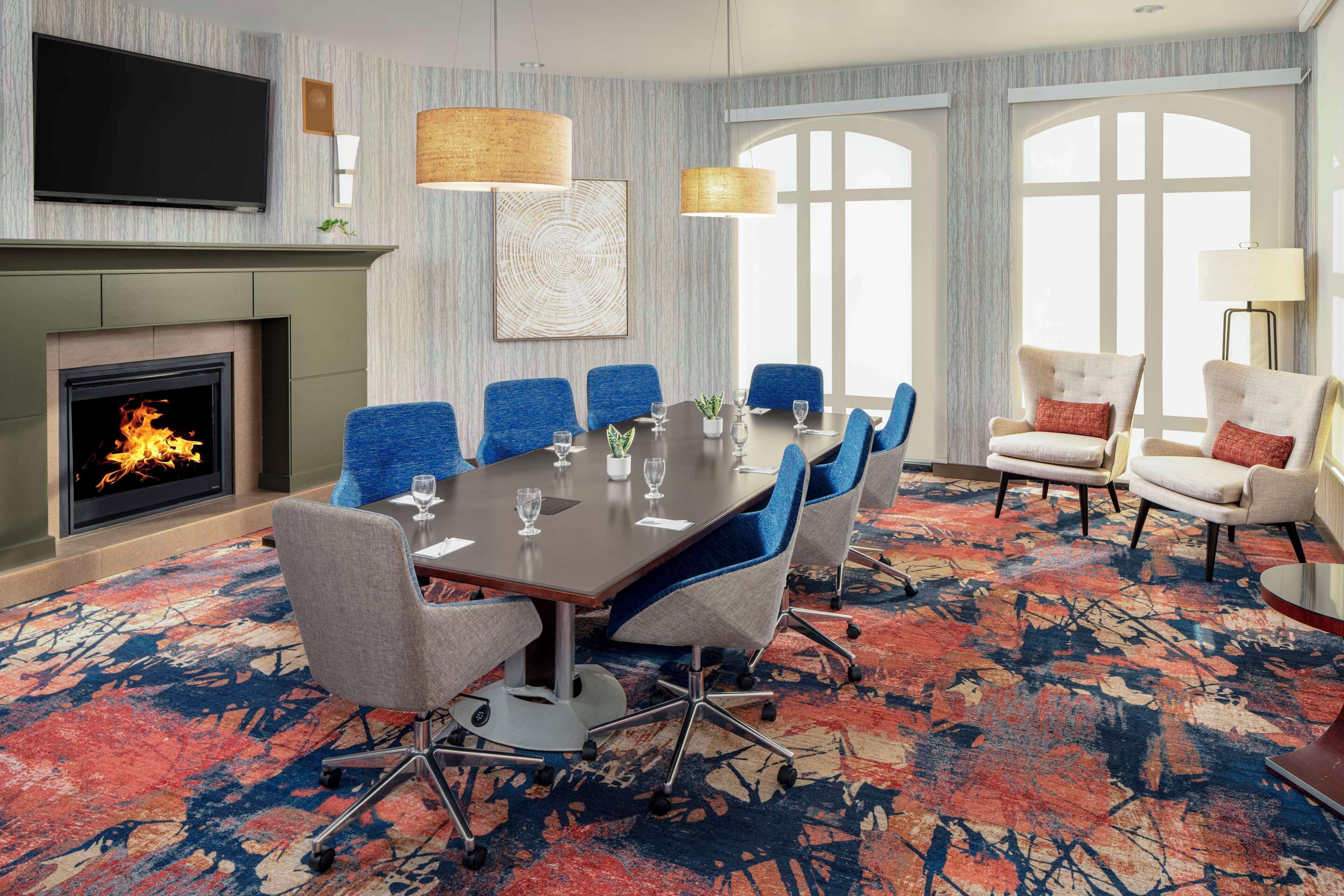 A conference room with a fireplace, a large table with chairs, and a TV mounted on the wall.