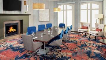 A conference room with a fireplace, a large table with chairs, and a TV mounted on the wall.