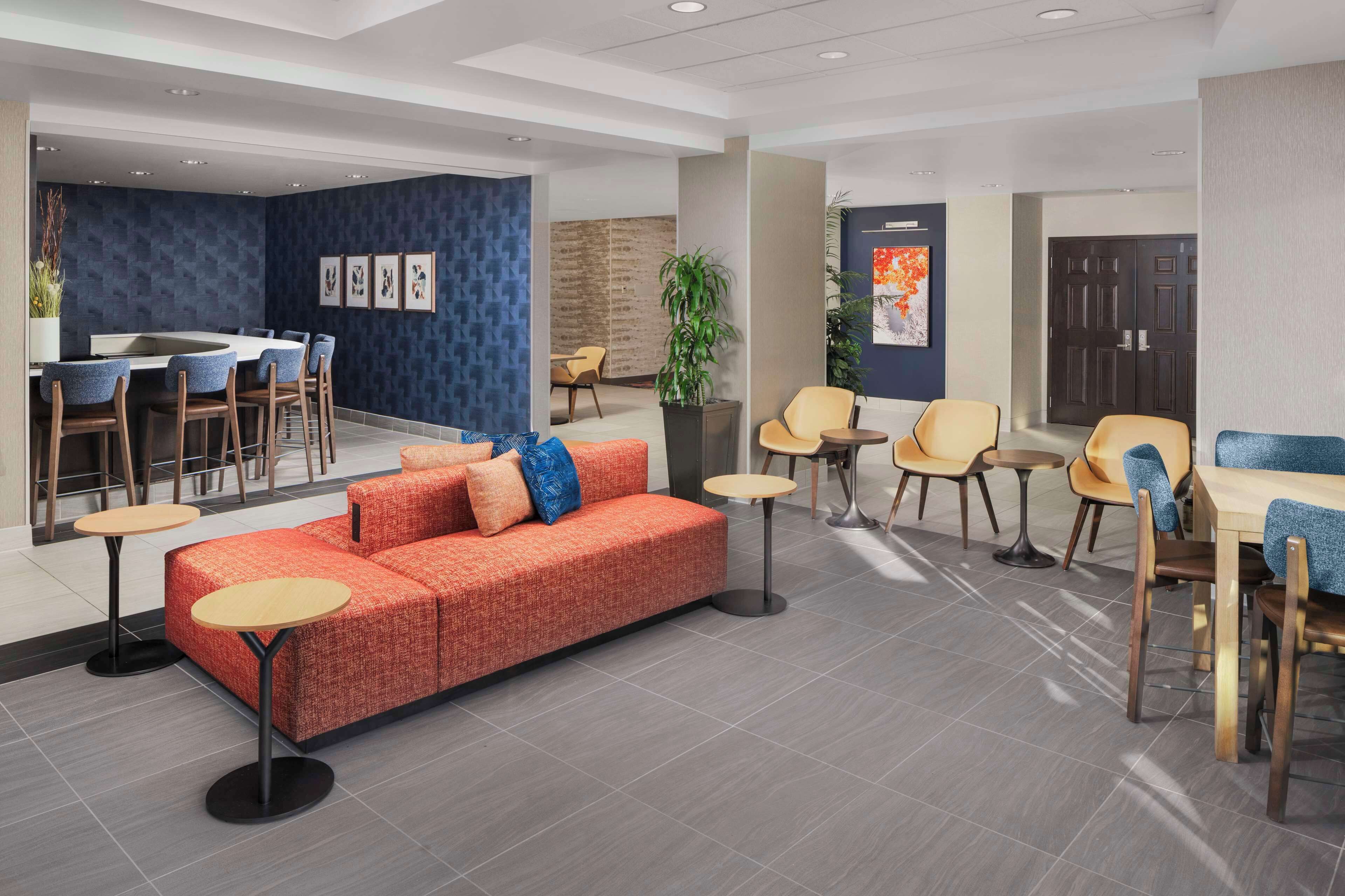 A modern lobby with a red sofa, multiple seating areas, a reception desk, and a large plant.