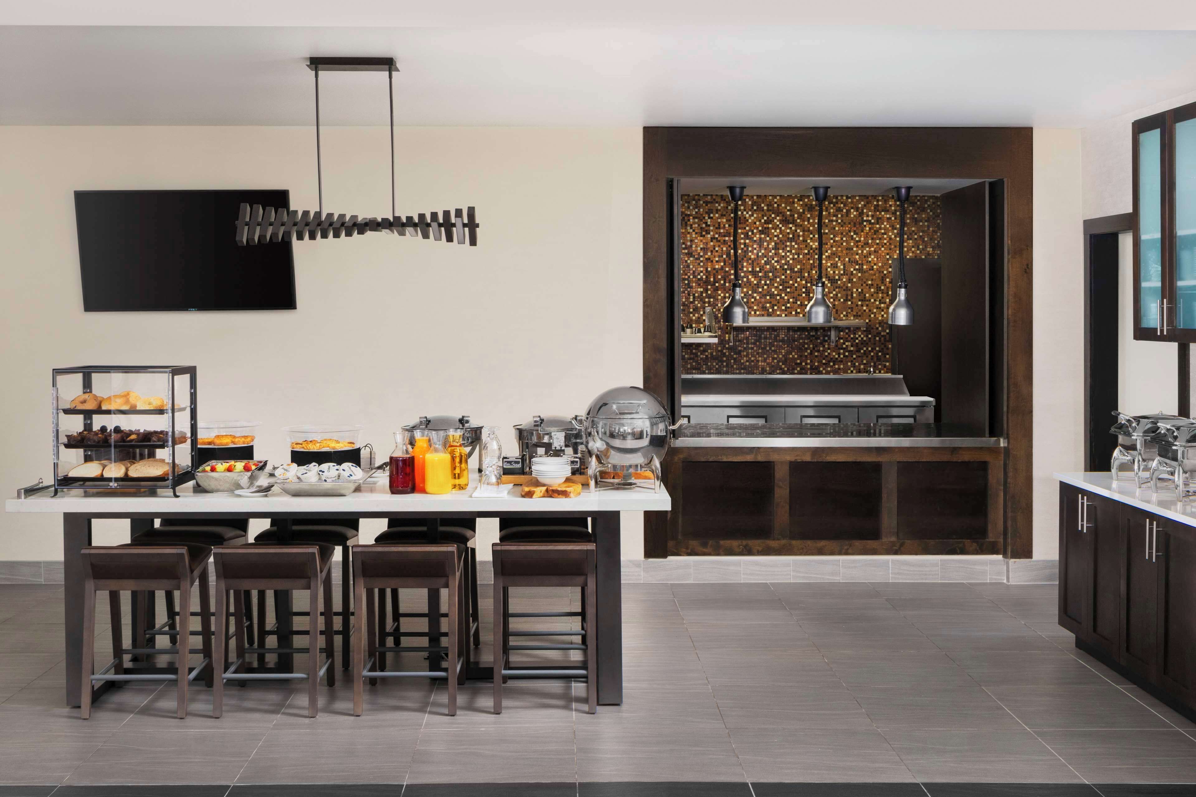 A modern kitchen with a central island, bar stools, a buffet setup, and a decorative wall panel.