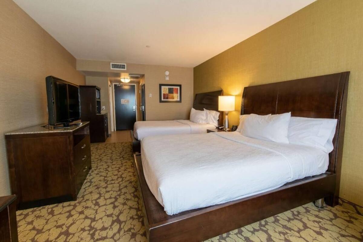A hotel room with a bed, a desk with a television, and a door leading to another room.