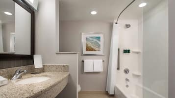 Un baño moderno con un lavabo de granito, un espejo grande, un cuadro enmarcado de una playa, un inodoro, una ducha y una bañera.