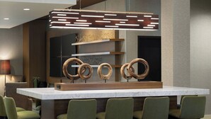 Zona de bar moderna con encimera de mármol, sillas tapizadas en verde y una lámpara de diseño único.