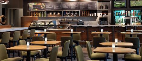 A modern bar area with multiple seating options, a counter with a menu board, and a television screen displaying a sports game.