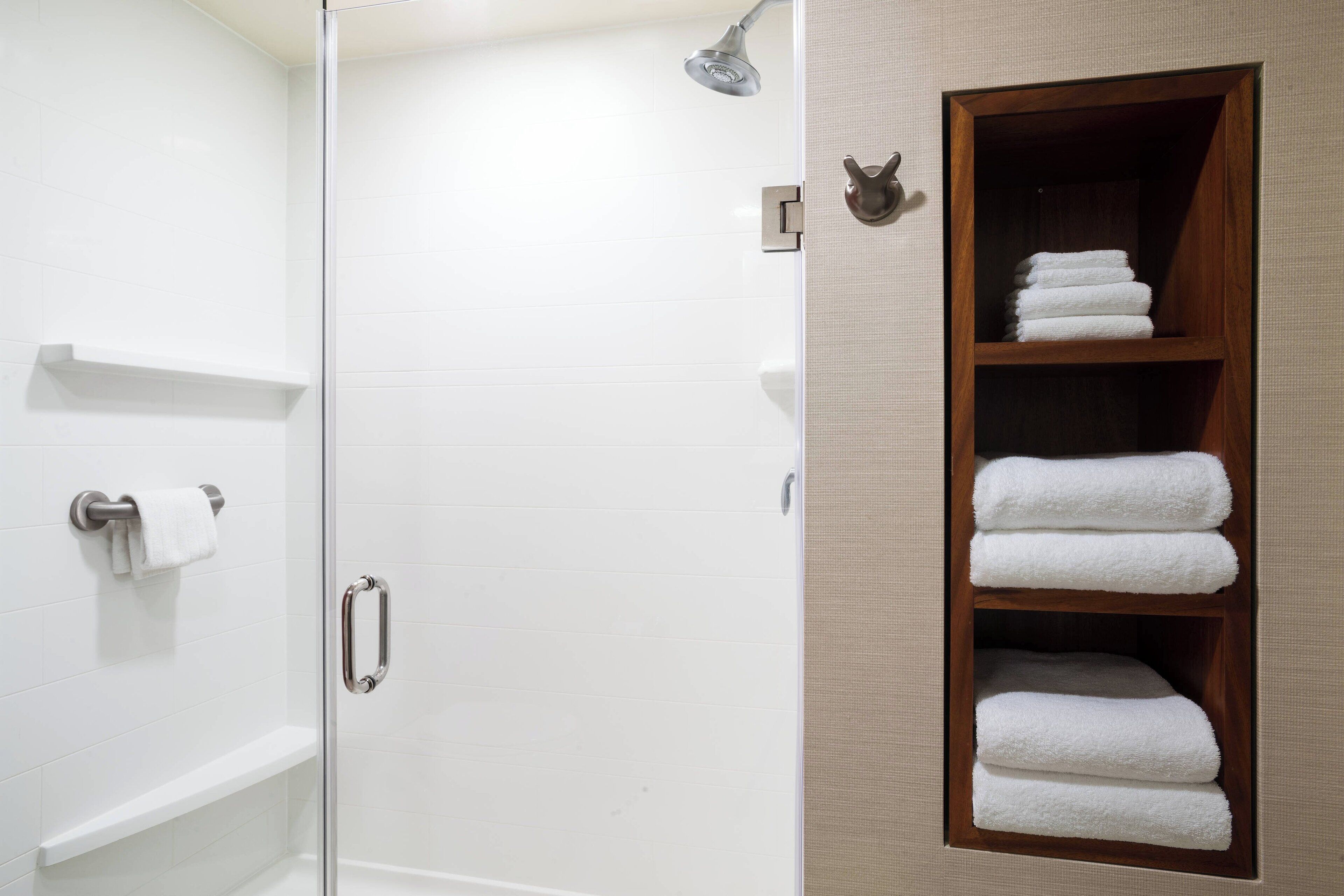 Ducha con puerta de cristal, toallero y estante de madera con toallas dobladas.