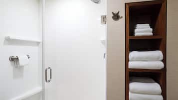 Ducha con puerta de cristal, toallero y estante de madera con toallas dobladas.