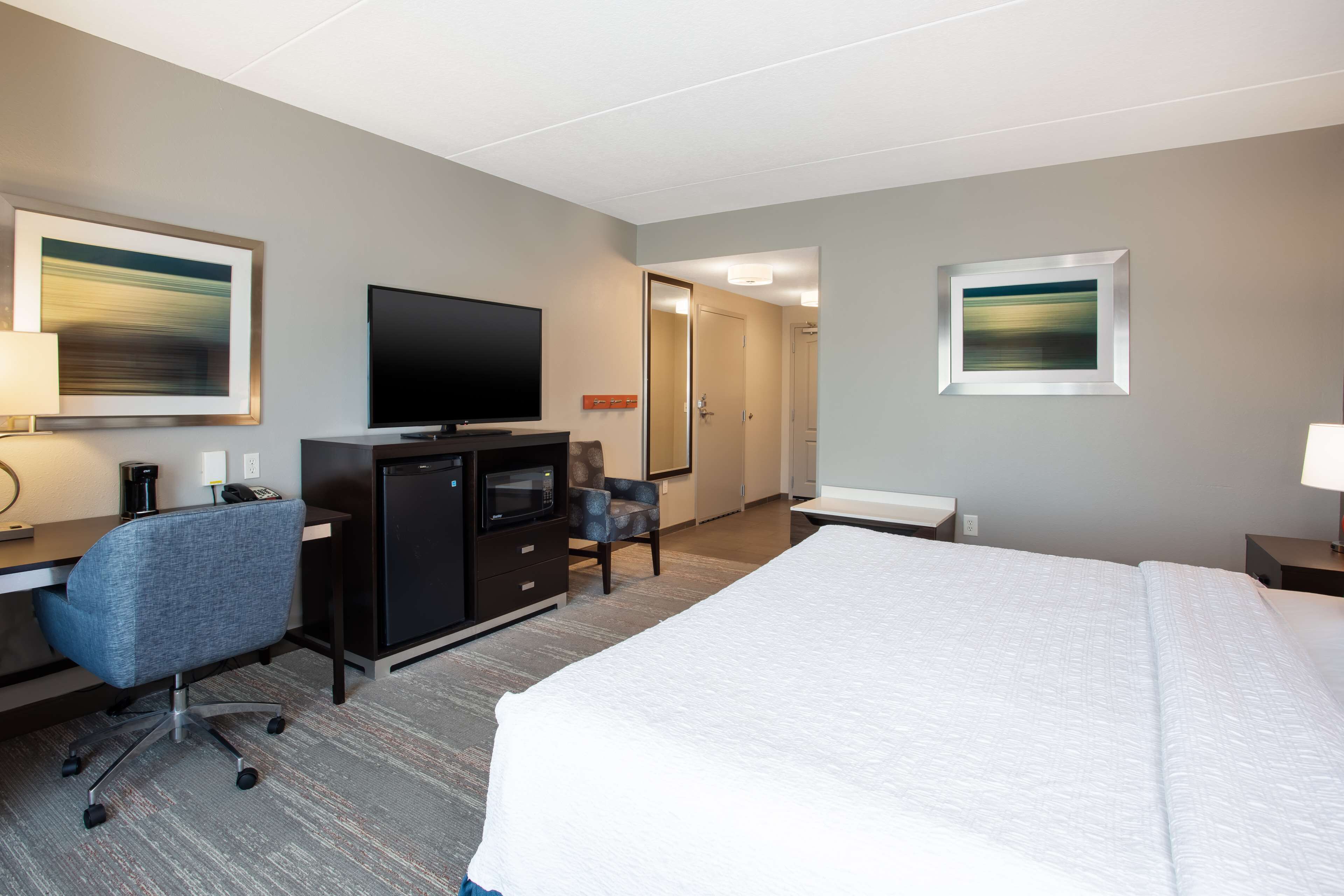 A hotel room with a bed, a desk with a computer, a television, a microwave, and a chair.