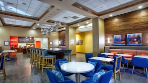 Un hall d’hôtel moderne avec des fauteuils bleus, des tables rondes, un bar central et un mur décoratif en bois.