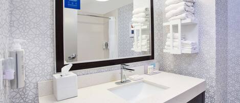 Un baño moderno con un espejo grande, un lavabo, un perchero para toallas y un dispensador de gel antibacterial.