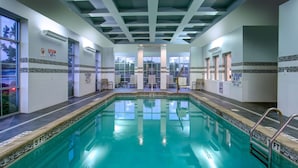 Une piscine intérieure à l’eau claire, entourée de murs et de fenêtres recouverts de carreaux.