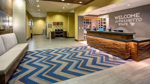 Un espace d’accueil avec un comptoir de réception en bois, un tapis à motifs chevrons bleus et oranges, et un mur orné d’une pancarte de bienvenue.