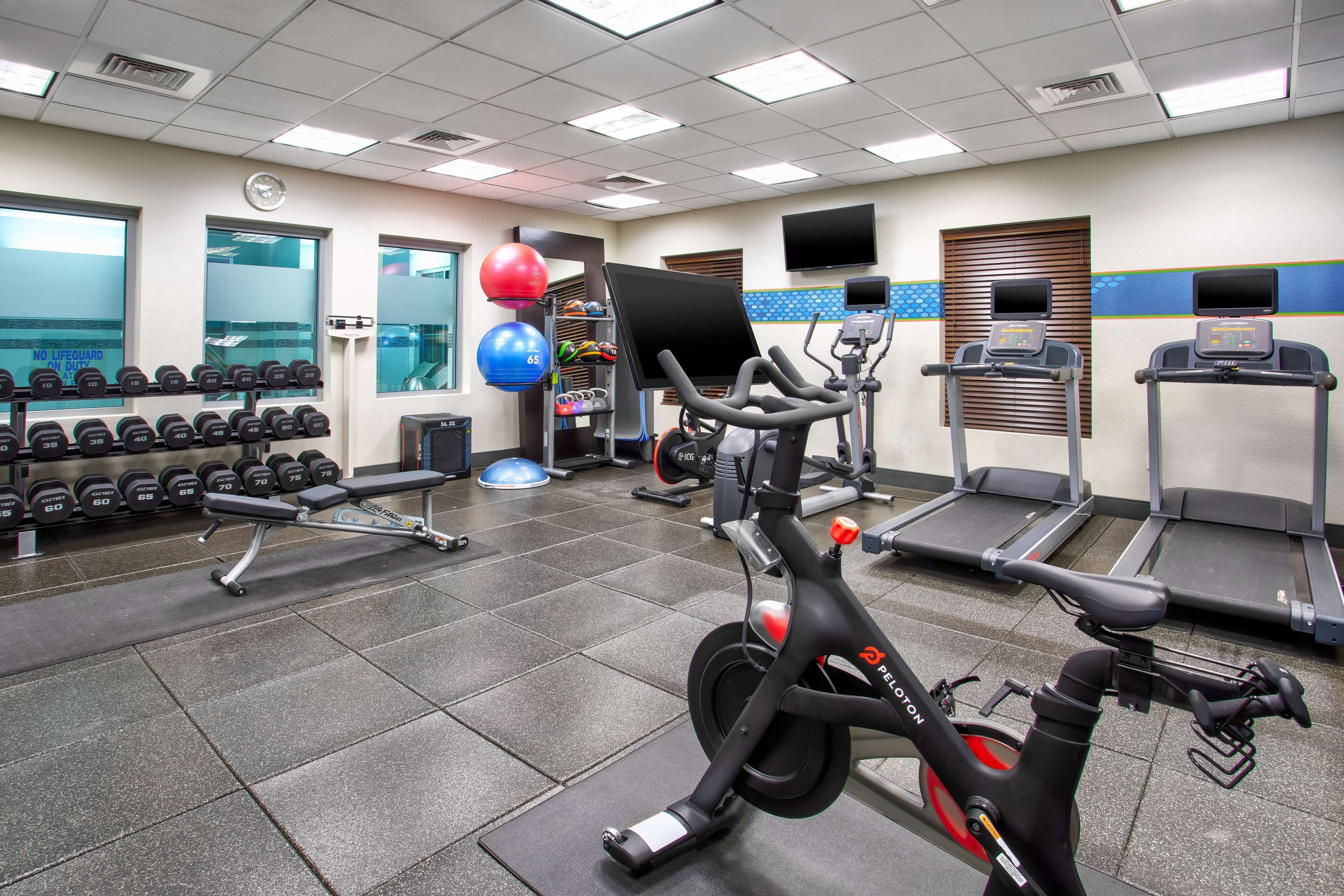 A gym with exercise equipment including dumbbells, a stationary bike, treadmills, and exercise balls.