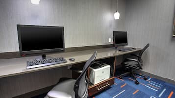 Et hotelkontor med to skriveborde, hver med computerskærm, tastatur og mus. To kontorstole, hvoraf den ene har en skrivebordsorganisator under bordet. Værelset har et tæppe med et geometrisk mønster og en lampe på væggen.