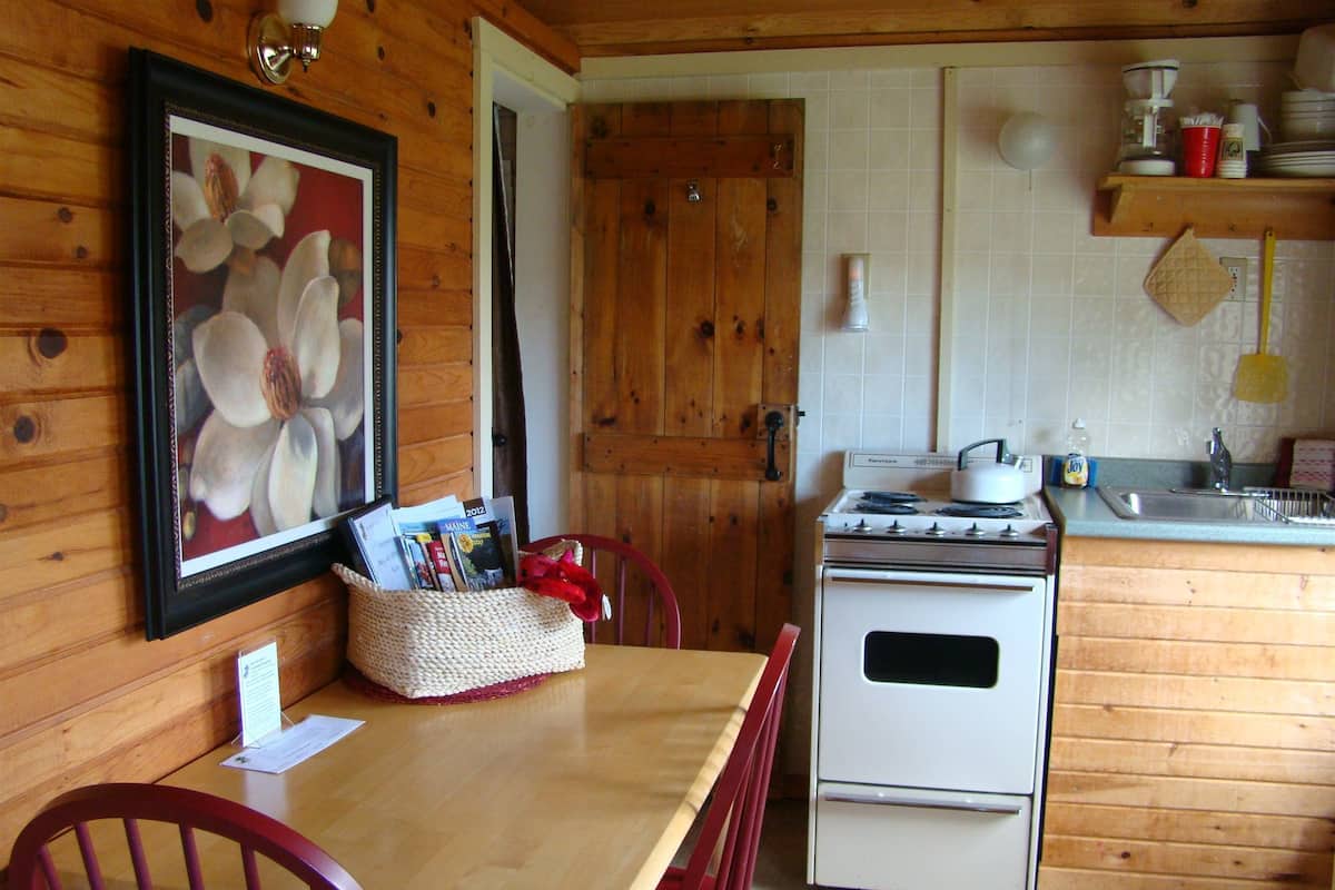 A wooden interior with a dining table, chairs, a stove, and a framed picture on the wall.