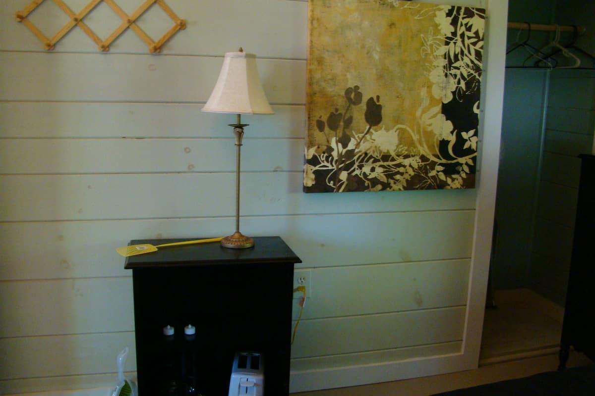 A room with a lamp on a black table, a painting on the wall, and a wooden wall decoration.