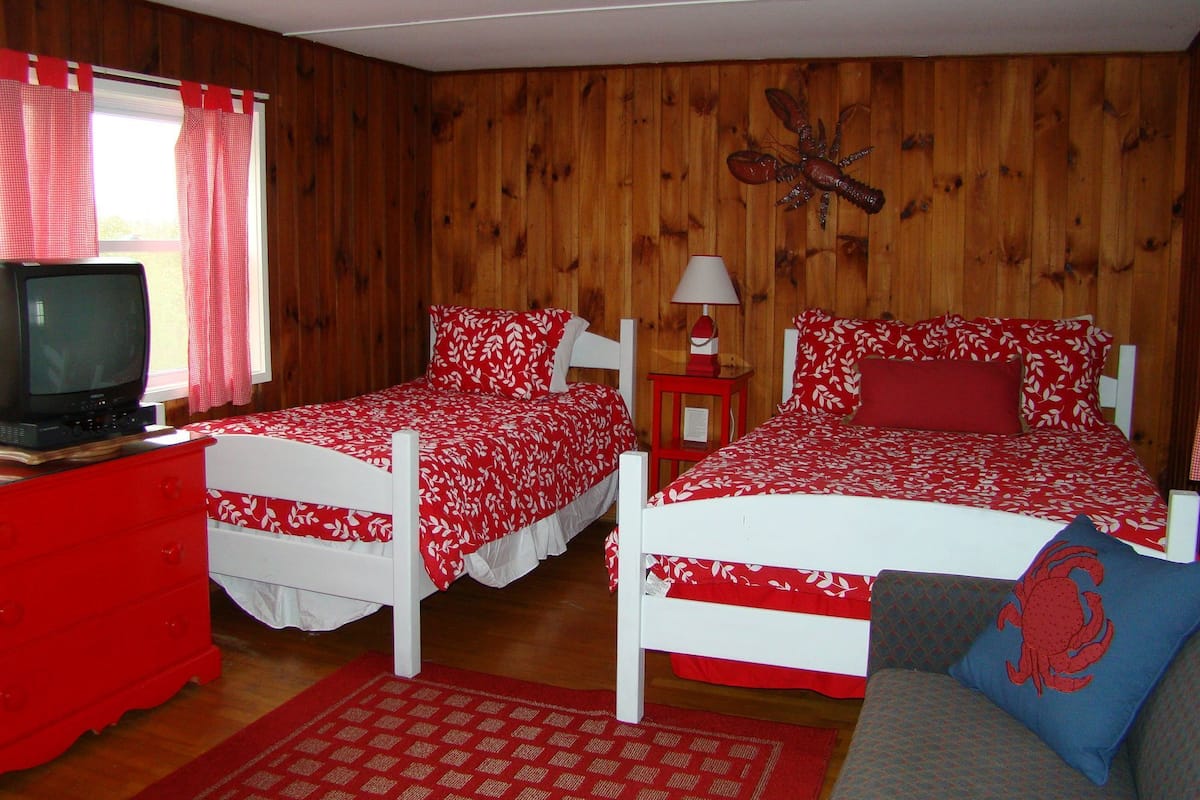 A room with two single beds, a red dresser, a television on a wooden cabinet, and a wooden wall with a decorative element.