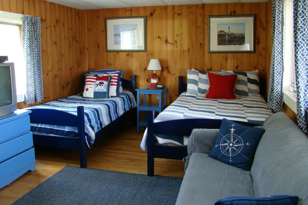 A room with two beds, a sofa, a TV, and wooden walls.