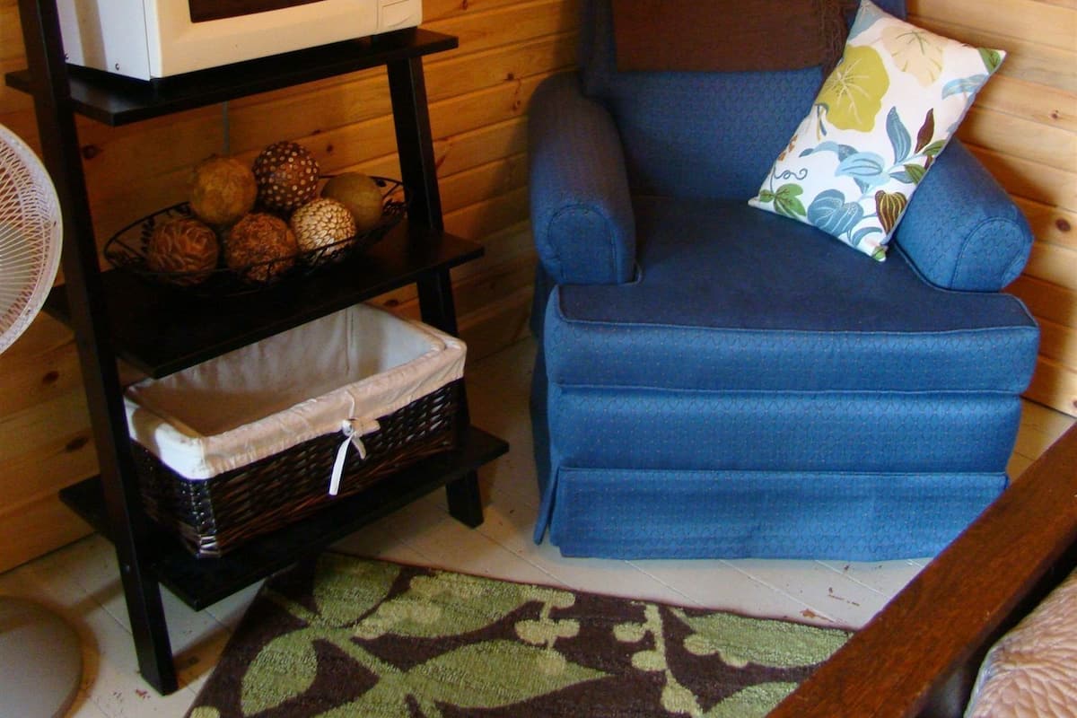 A cozy room with a blue armchair, a microwave on a shelf, a fan, and a decorative plant.