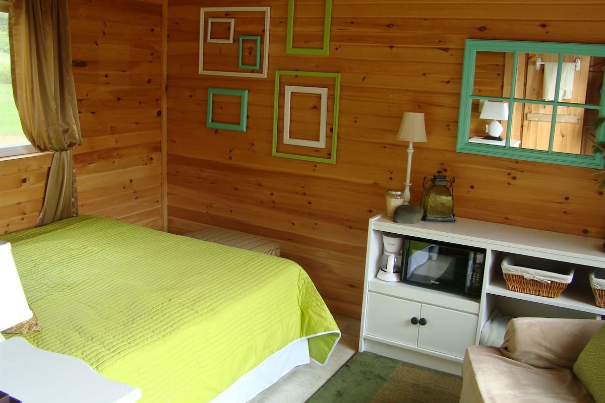 A wooden cabin room with a bed, a white dresser, and a mirror.