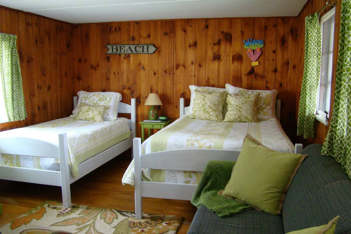 A room with two single beds, a sofa, and a wooden wall with a 'BEACH' sign.