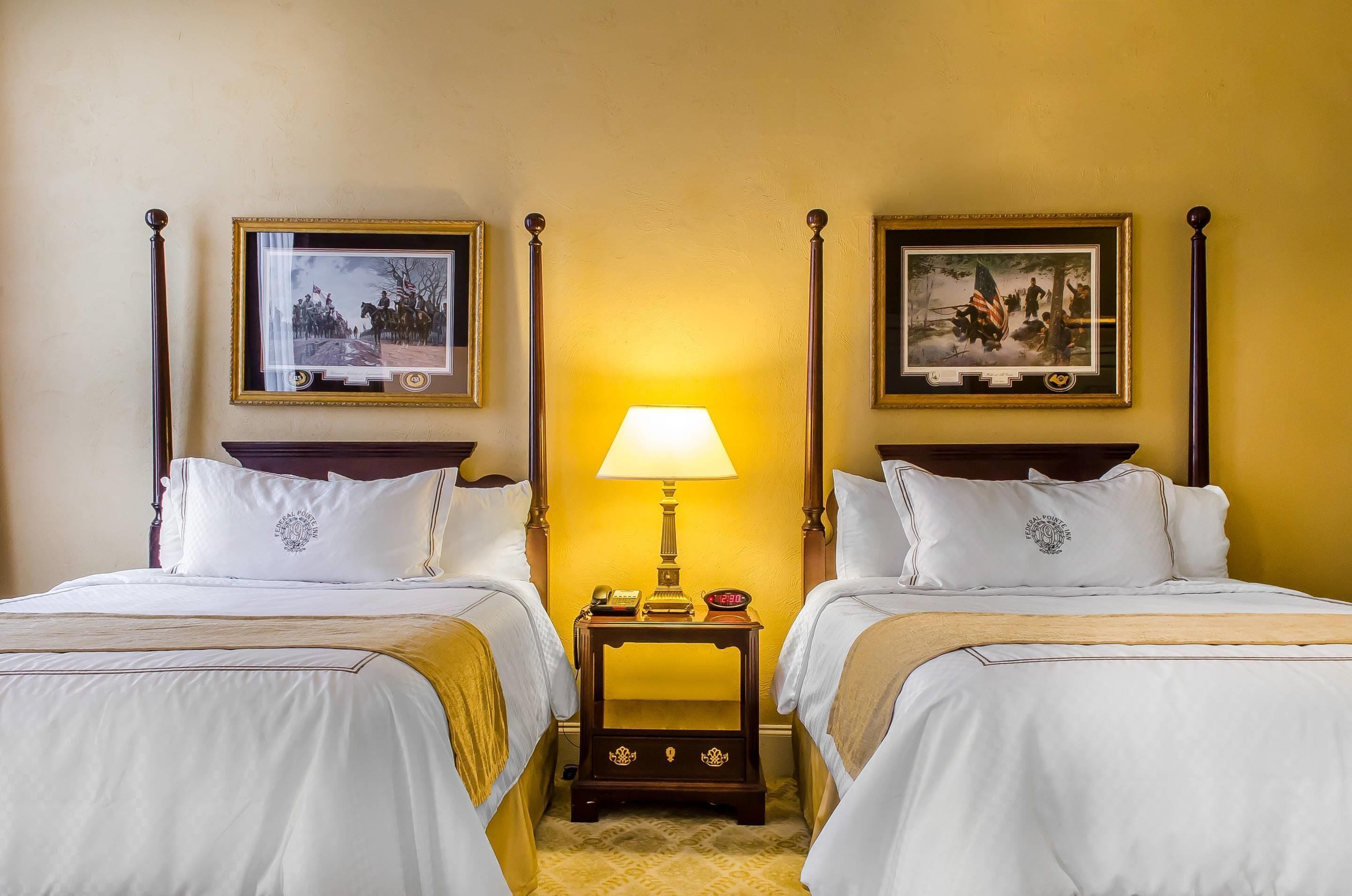 Une chambre d’hôtel avec deux lits, une table de chevet avec une lampe et des tableaux encadrés aux murs.