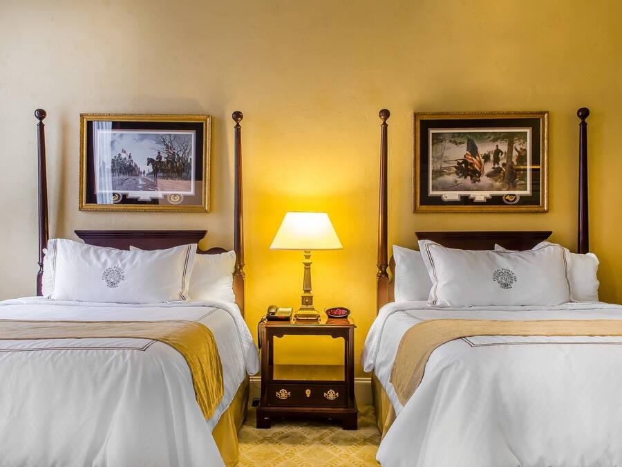 Une chambre d’hôtel avec deux lits, une table de chevet avec une lampe et des tableaux encadrés aux murs.