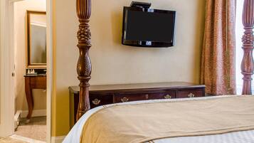 Ein Hotelzimmer mit Himmelbett, Flachbildfernseher an der Wand, einem hölzernen Schminktisch mit Schubladen und einem Spiegel in der Ecke.