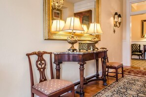 A wooden chair with a cushioned seat, a console table with a lamp, and a mirror with a gold frame.
