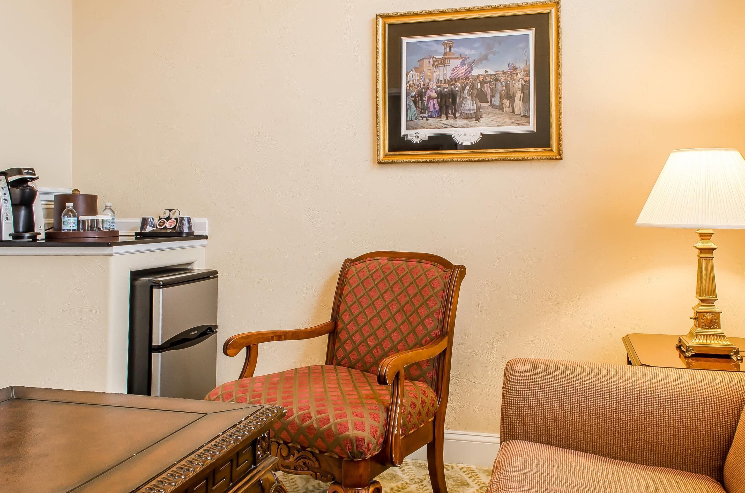 A room with a dining table, a refrigerator, a chair, a sofa, a lamp, and a framed picture on the wall.