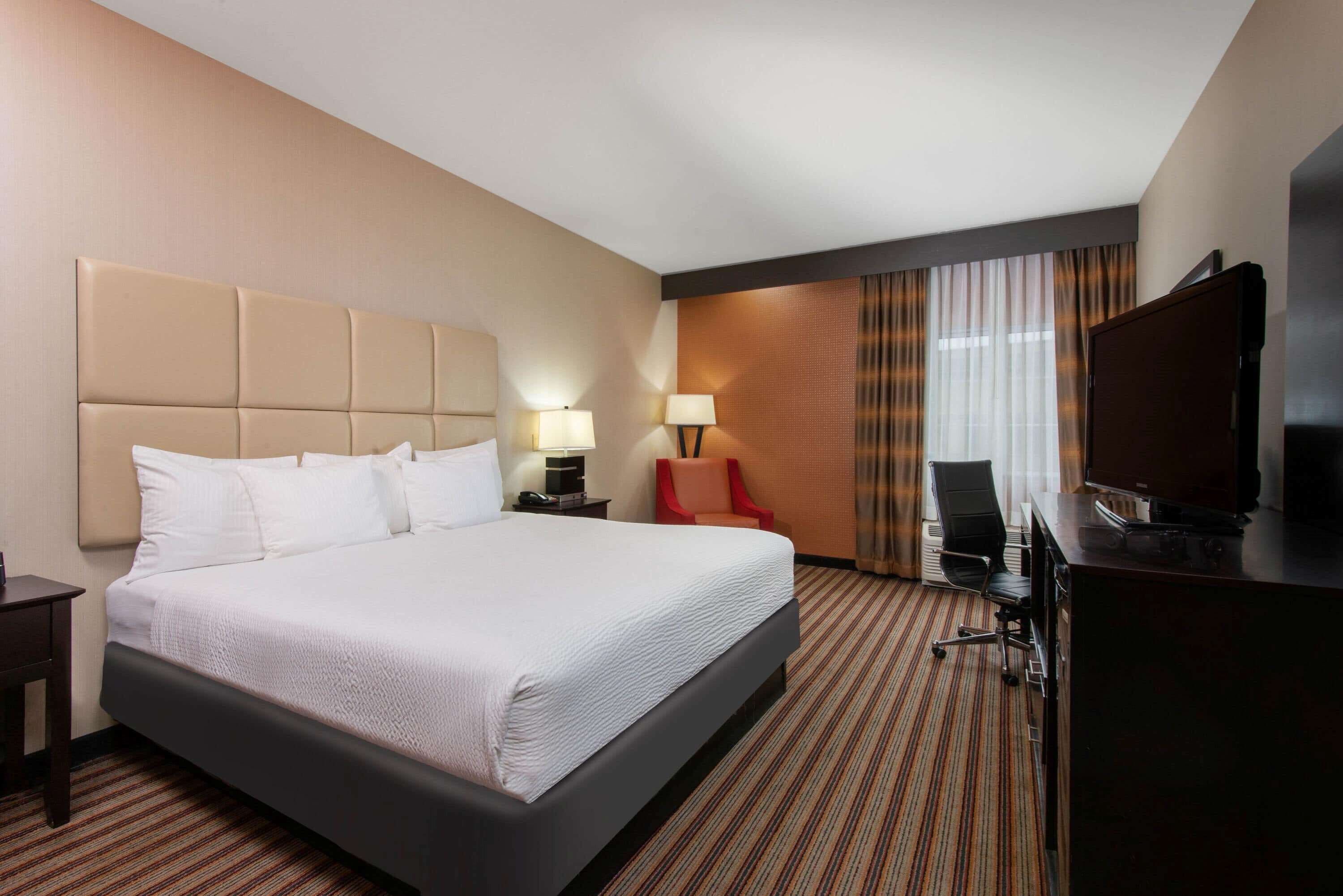 Una habitación de hotel con una cama grande, un escritorio con computadora, un televisor y una silla.