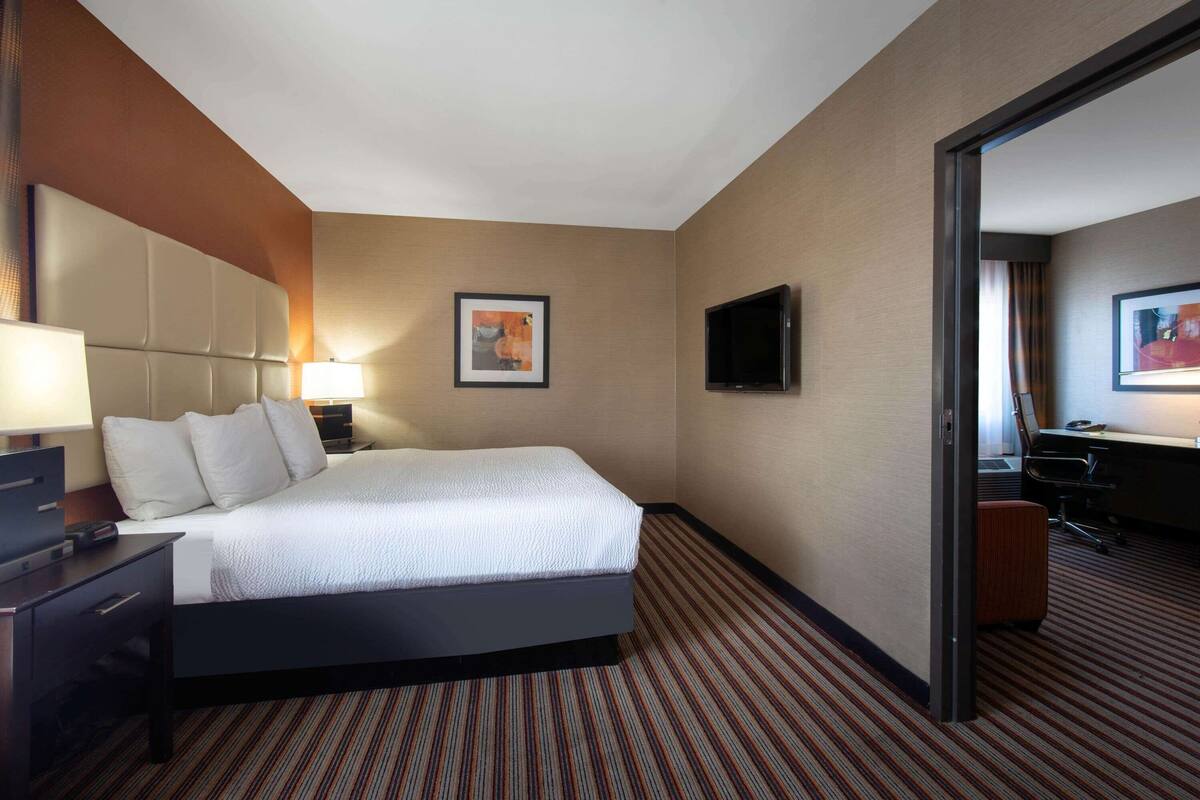 A hotel room with a large bed, a desk with a lamp, a flat-screen TV, and a framed picture on the wall.