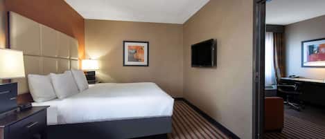 A hotel room with a large bed, a desk with a lamp, a flat-screen TV, and a framed picture on the wall.