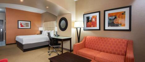 A hotel room with a bed, a desk, a chair, a sofa, and two framed artworks on the wall.