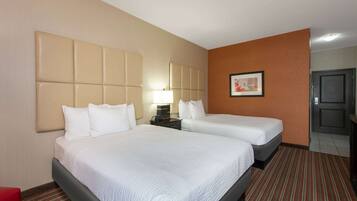 A hotel room with two beds, a nightstand with a lamp, a framed picture on the wall, and a door to the right.