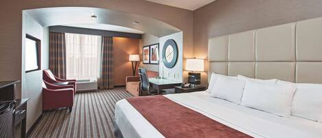 A hotel room with a large bed, a desk, a chair, and a TV.