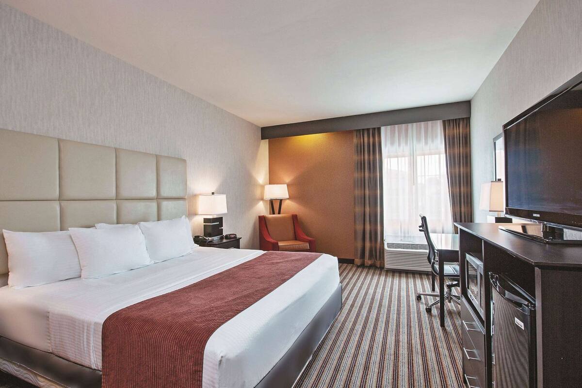 A hotel room with a large bed, a desk with a television, a chair, and a window with curtains.
