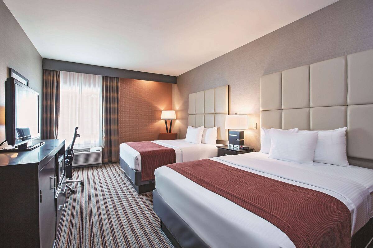 A hotel room with two beds, a desk, a chair, and a TV.