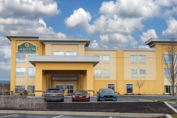 Edificio de La Quinta Inn & Suites con fachada amarilla, estacionamiento con tres coches y cielo despejado con nubes.
