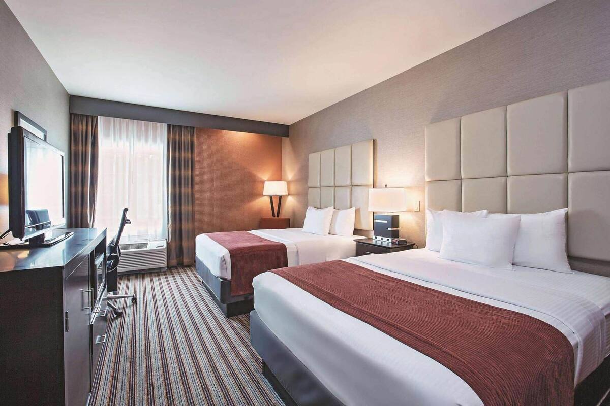 A hotel room with two beds, a desk, a television, and a window with curtains.