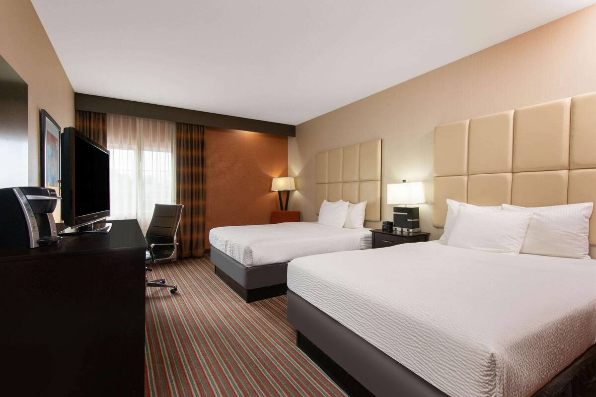 A hotel room with two beds, a desk, a television, and a window with curtains.