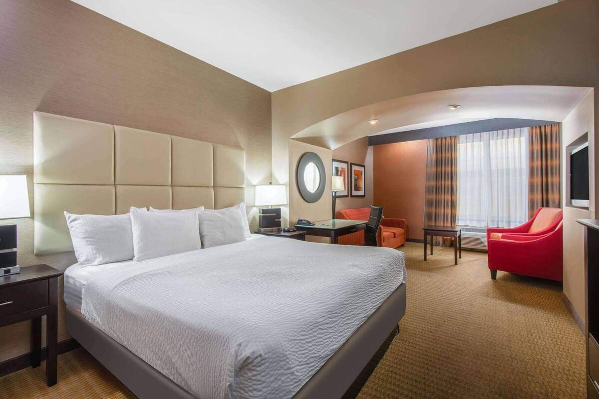 A hotel room with a large bed, a desk, a chair, a TV, and a separate seating area with curtains.
