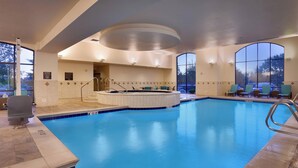 Een groot binnenzwembad met een jacuzzi, een zitgedeelte en uitzicht op de omgeving.