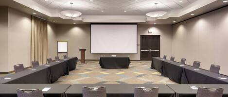 A conference room with a long table, chairs, a projector screen, and a podium.