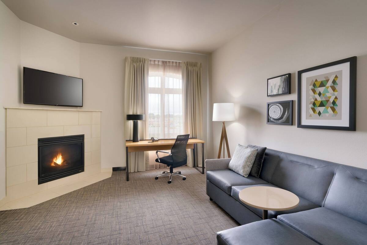 Une chambre d’hôtel moderne dotée d’une cheminée, d’un téléviseur à écran plat, d’un bureau, d’un canapé confortable et d’une petite table ronde.