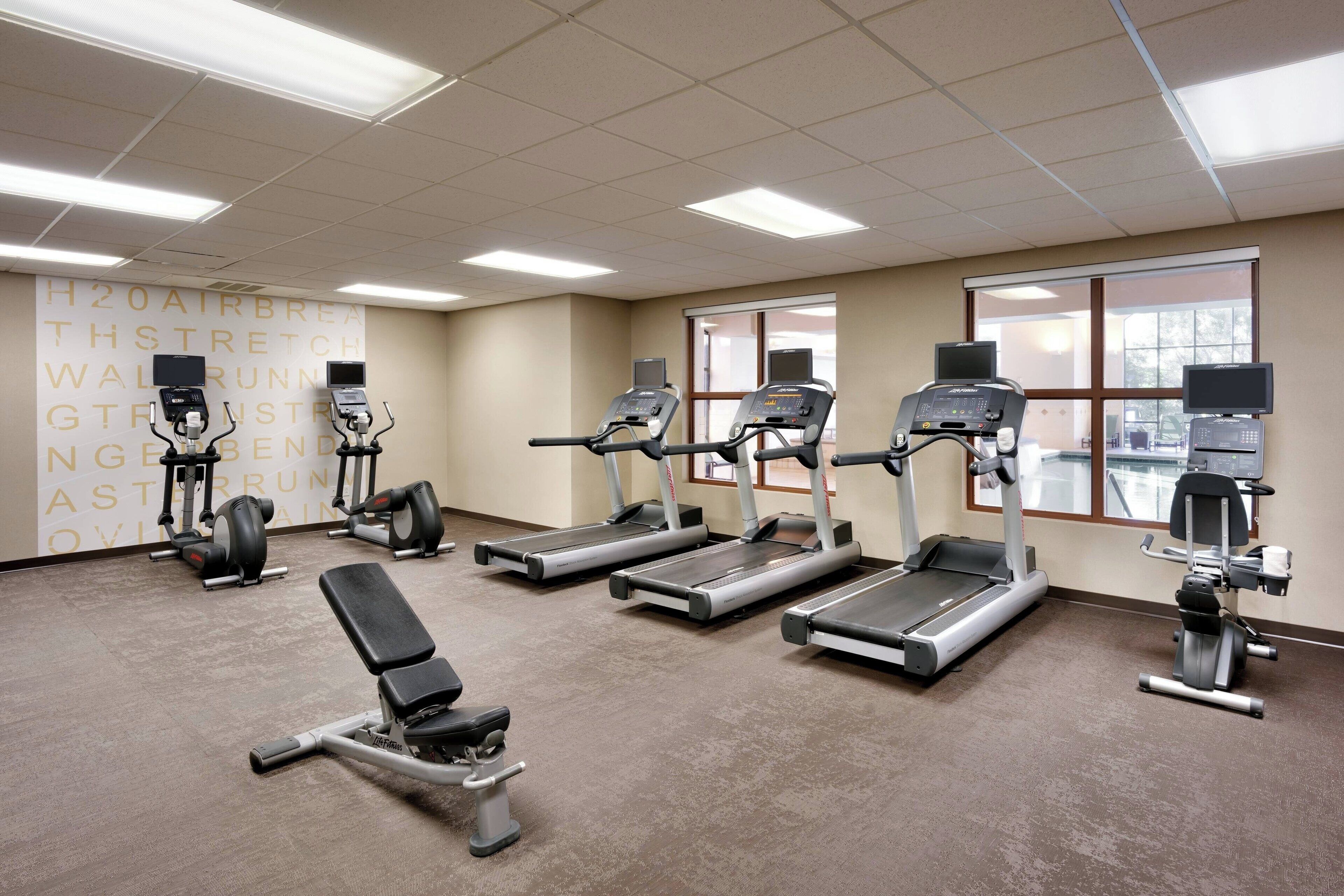 A gym with treadmills, elliptical machines, and a bench.