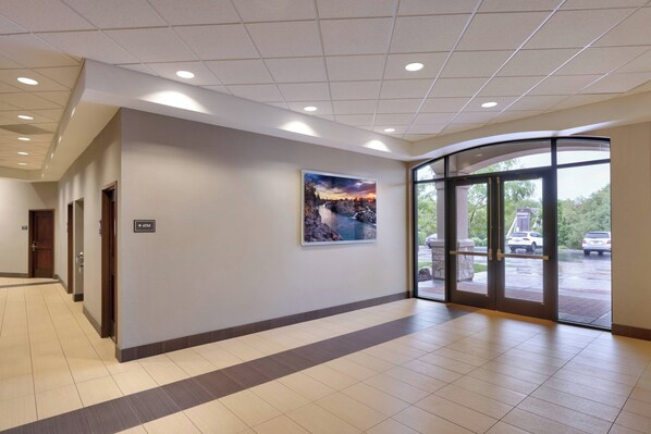A spacious lobby with a large glass door entrance, a view of the outdoors, and a sign indicating an ATM.
