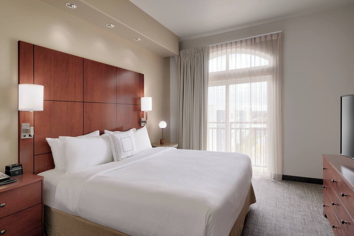 Une chambre d’hôtel avec un grand lit, une tête de lit en bois, deux lampes de chevet, une commode et un téléviseur.
